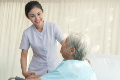 cheerful asian caregiver smiling to the camera while holding the old lady