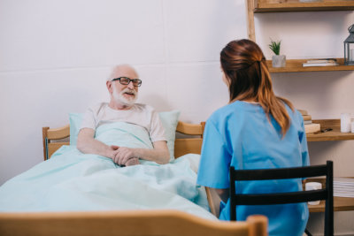 smiling old patient in bed talking to caregiver